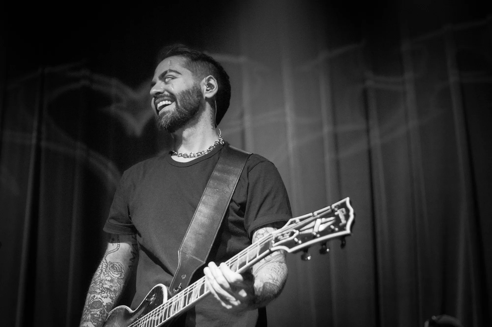 A black and white image of Kourosh Zarandooz, Aemia's lead guitarist, smiling as he performs.