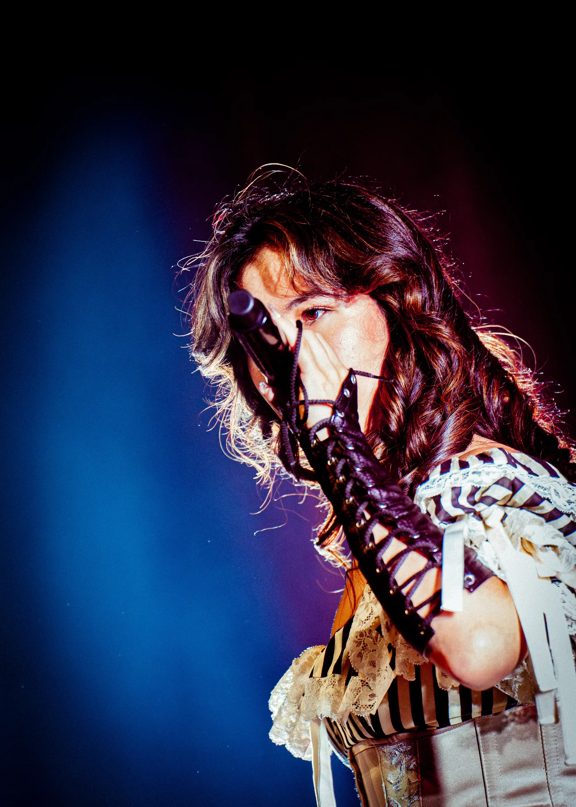 Close-up of Emei singing into a handheld microphone, framed by blue and red stage lighting.