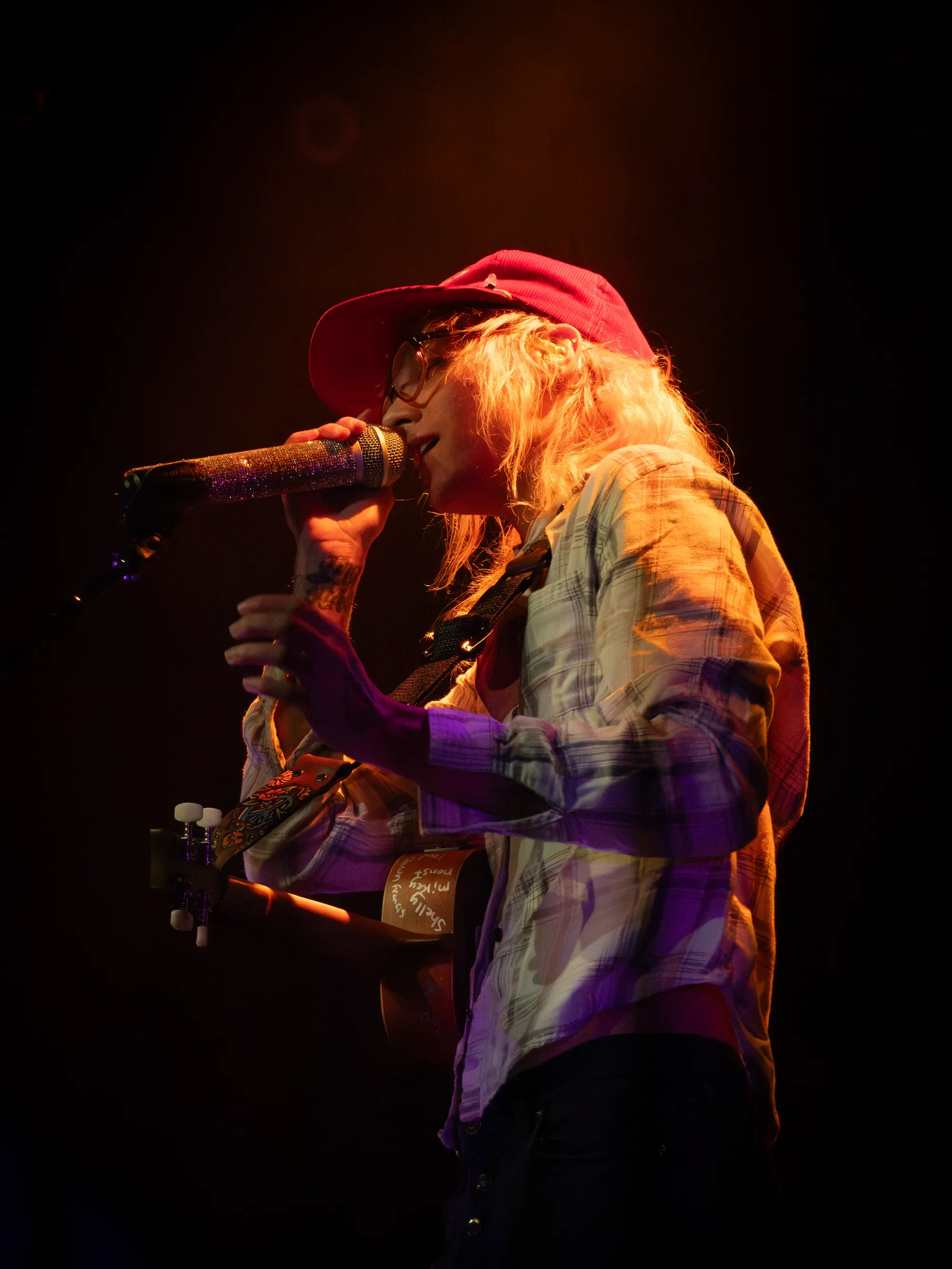 Brake sings into a microphone while playing guitar under amber and purple lighting at The Pearl.