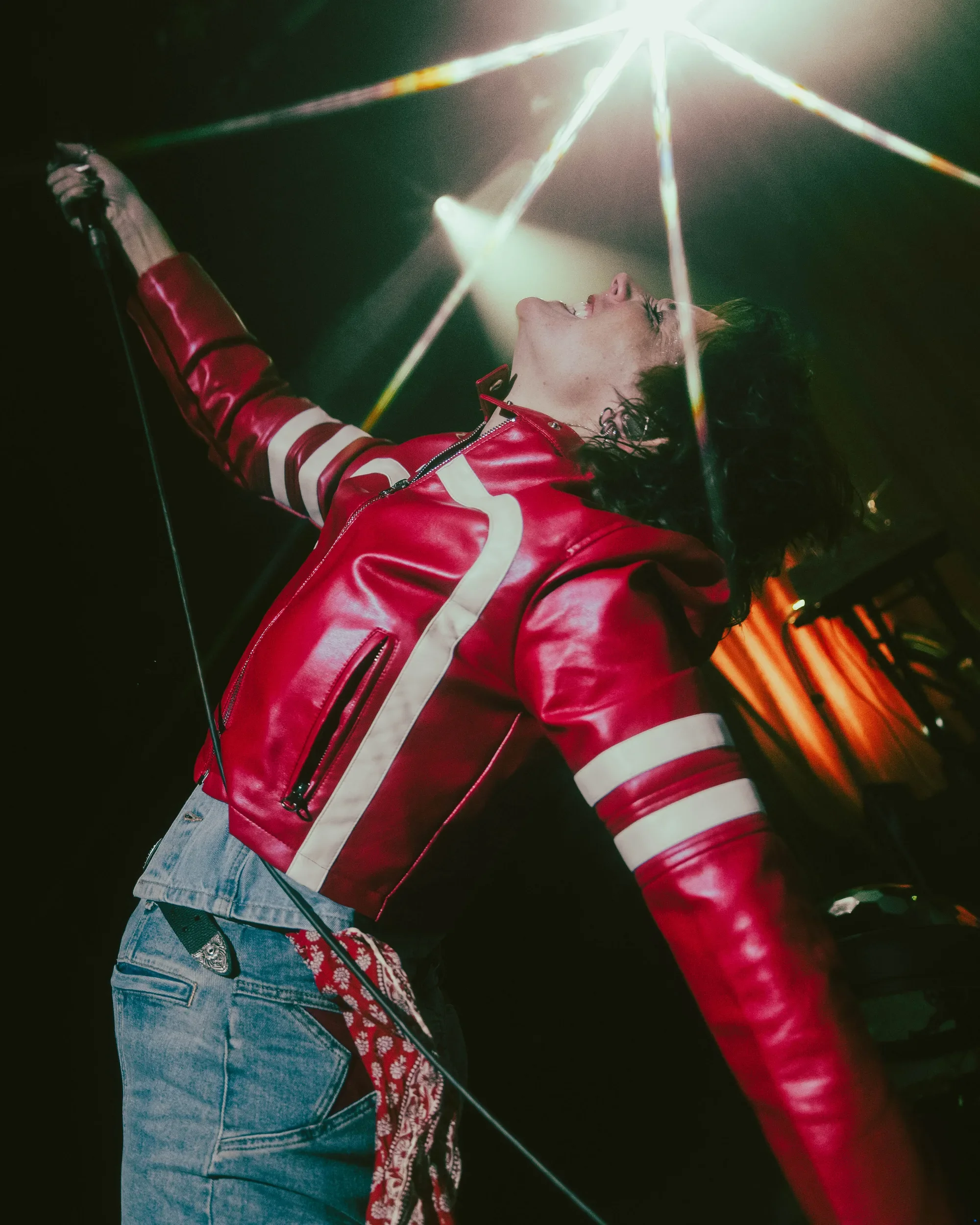 Sammy Rae leaning back in a red jacket beneath starburst stage lights.