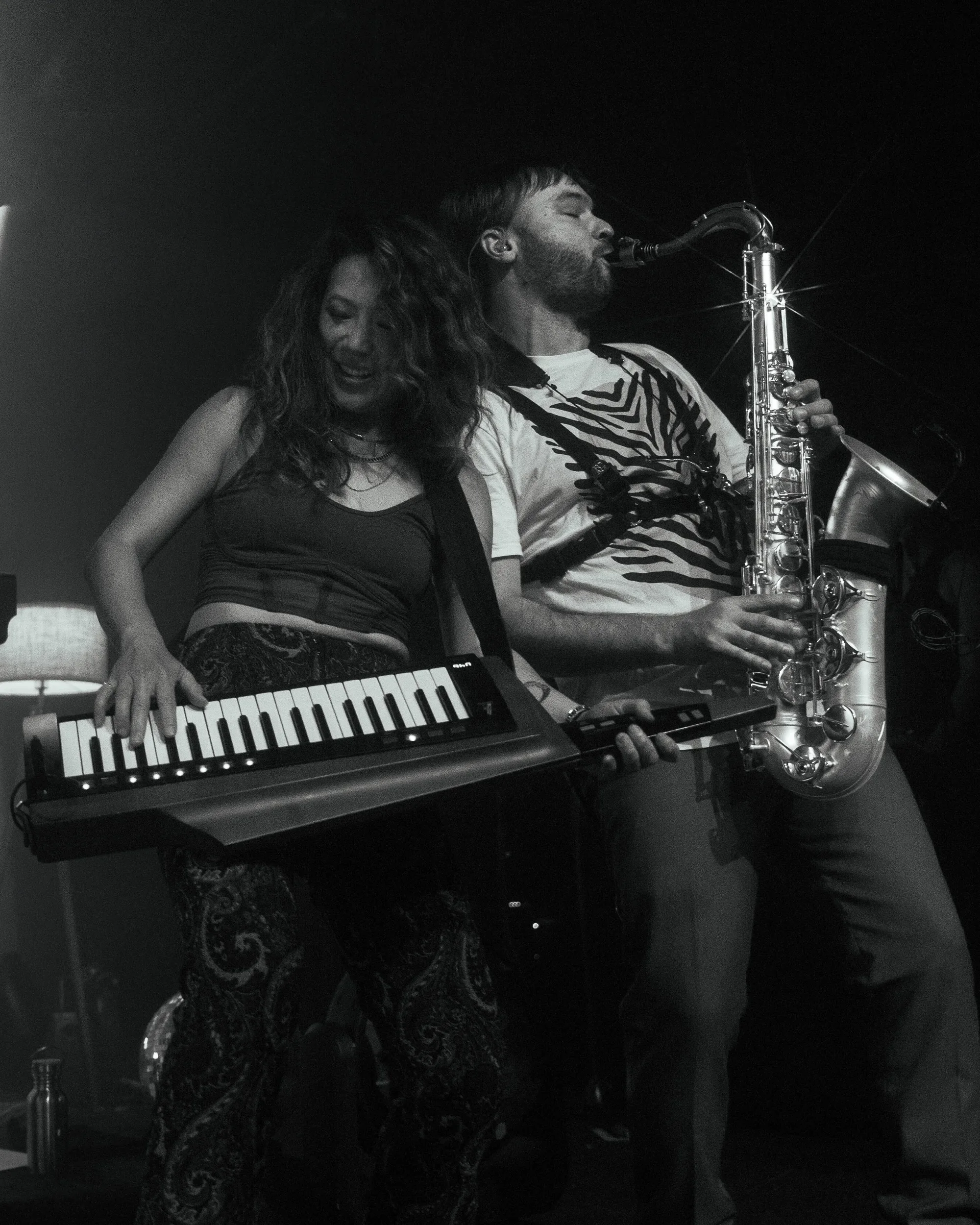 A keyboardist and saxophonist performing side by side in black and white.